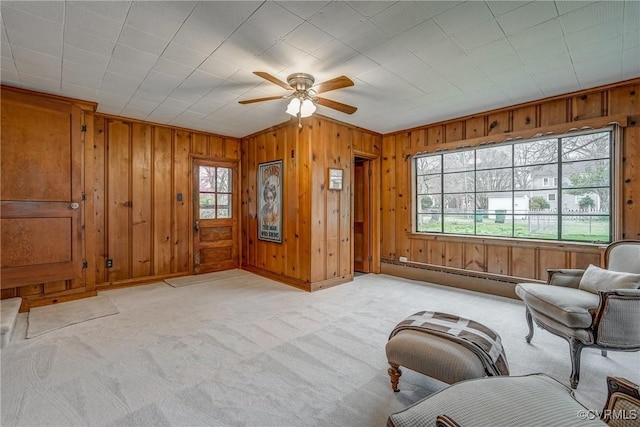 unfurnished room featuring wood walls, baseboard heating, baseboards, light colored carpet, and ceiling fan