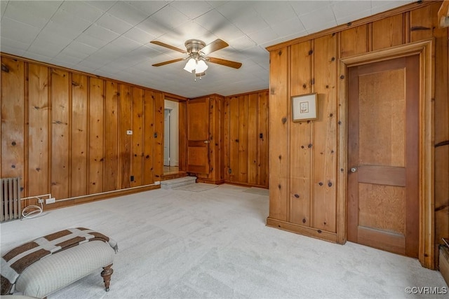 bedroom featuring radiator, light carpet, wood walls, and baseboards