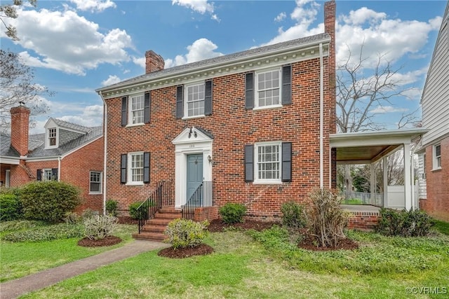 view of front facade with a chimney, a front lawn, and brick siding