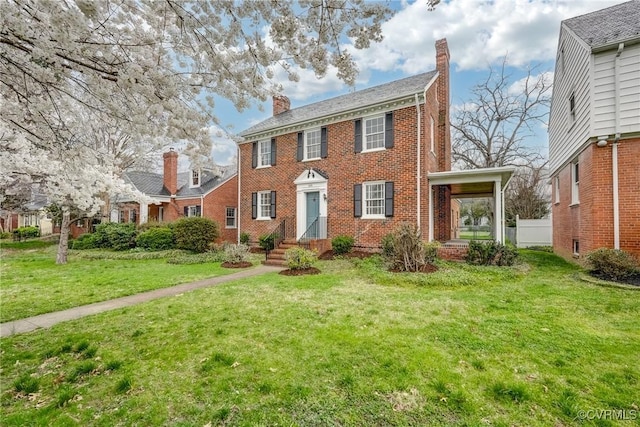colonial inspired home with brick siding, a front yard, and a chimney