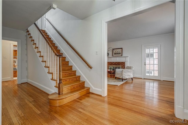staircase with baseboards, a fireplace, ornamental molding, and hardwood / wood-style flooring