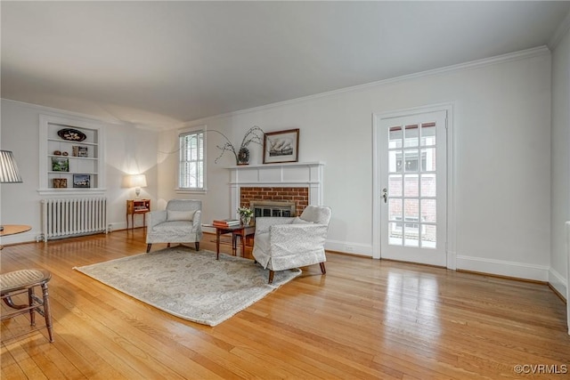 living area featuring radiator heating unit, a brick fireplace, crown molding, and light wood finished floors
