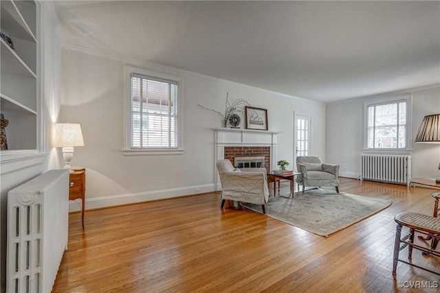 living room featuring radiator heating unit, a brick fireplace, ornamental molding, and light wood-style floors