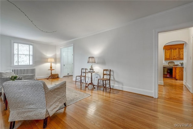sitting room featuring radiator, ornamental molding, baseboards, arched walkways, and light wood-style flooring