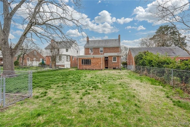rear view of property featuring brick siding, a chimney, a fenced backyard, and a yard