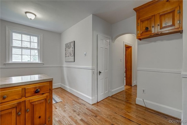 kitchen with light countertops, light wood-type flooring, baseboards, arched walkways, and brown cabinets