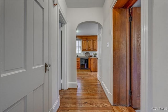 hall with arched walkways, baseboards, and light wood-type flooring