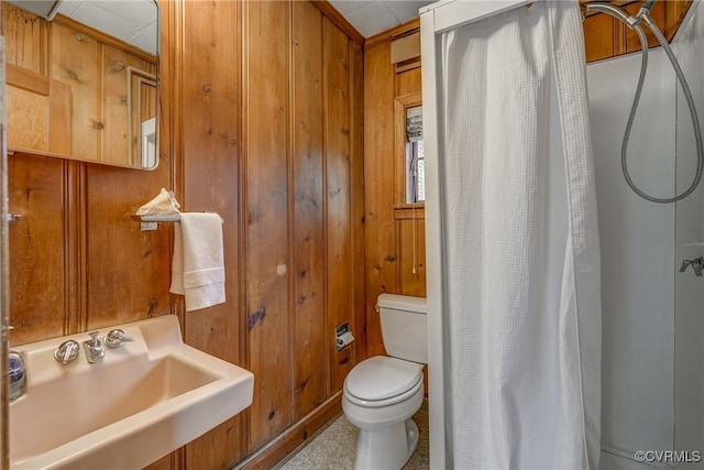 bathroom featuring toilet, a sink, a shower with shower curtain, and wooden walls