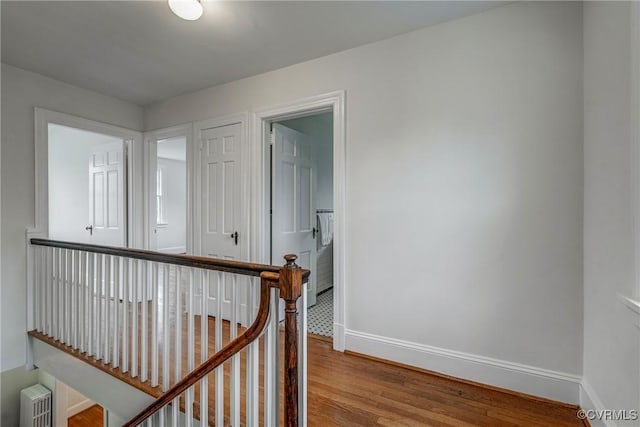 hallway with an upstairs landing, baseboards, and wood finished floors
