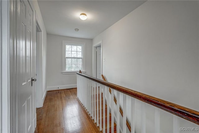 corridor with baseboards, an upstairs landing, and light wood-style floors
