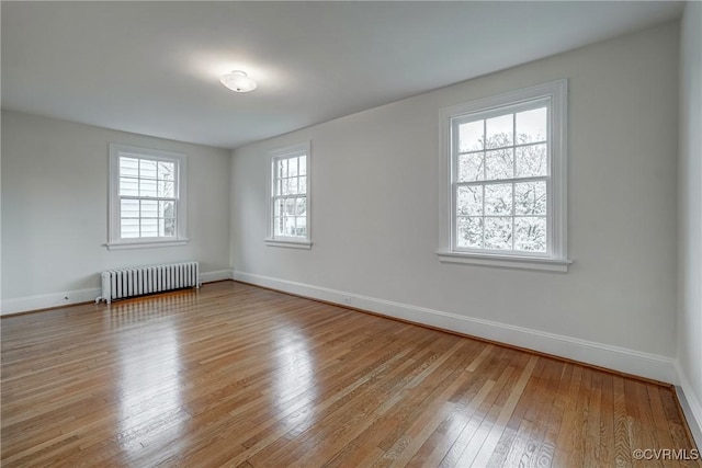 unfurnished room featuring radiator, light wood-style floors, and baseboards