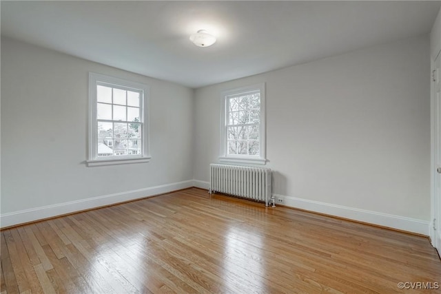 unfurnished room featuring radiator heating unit, plenty of natural light, baseboards, and light wood-type flooring