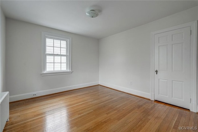 unfurnished room featuring baseboards, radiator heating unit, and light wood finished floors