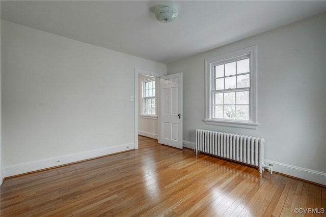 empty room with radiator heating unit, light wood-style flooring, baseboards, and a healthy amount of sunlight