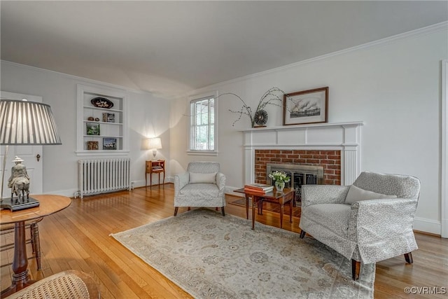 living area with radiator heating unit, ornamental molding, hardwood / wood-style flooring, and a fireplace