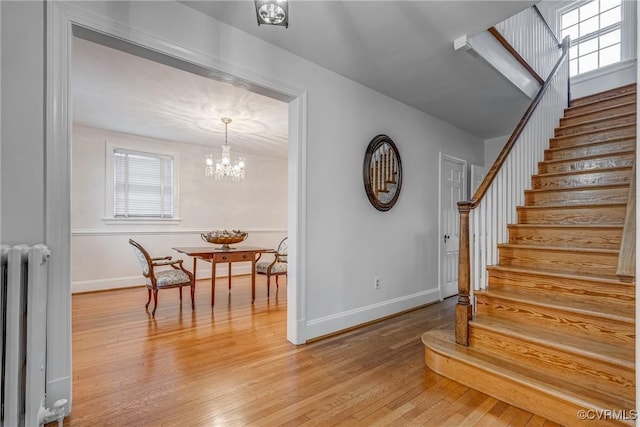 stairs featuring baseboards, wood finished floors, radiator heating unit, and a chandelier