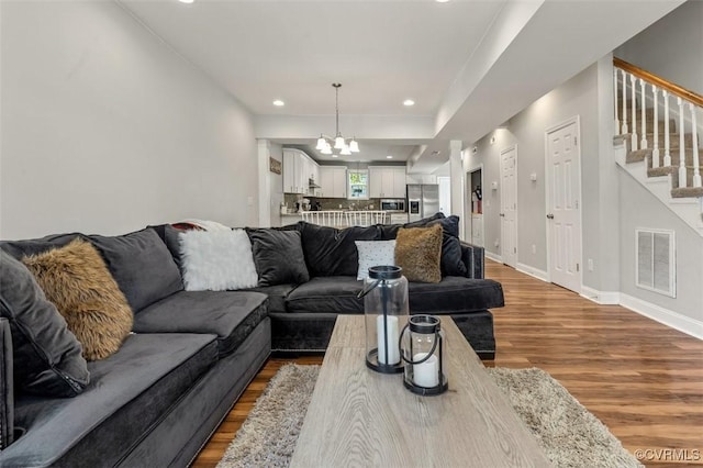 living area with a chandelier, stairs, baseboards, wood finished floors, and visible vents