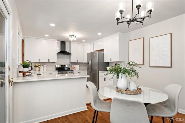 kitchen with wall chimney range hood, light countertops, a chandelier, wood finished floors, and stainless steel appliances