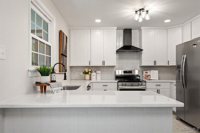 kitchen with a peninsula, wall chimney range hood, a sink, stainless steel appliances, and backsplash