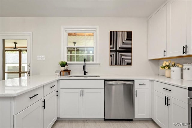 kitchen with a peninsula, dishwasher, a sink, and white cabinetry