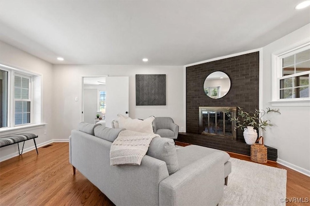 living room with visible vents, recessed lighting, wood finished floors, a brick fireplace, and baseboards
