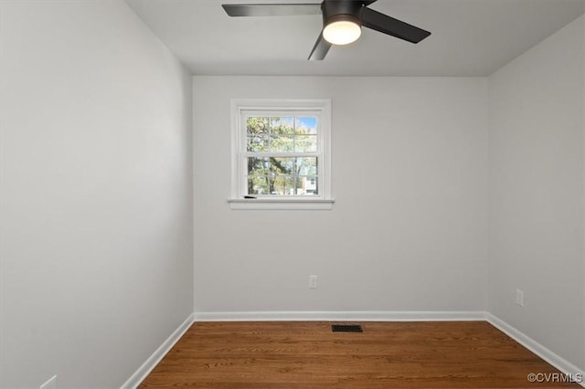 empty room with wood finished floors, ceiling fan, baseboards, and visible vents