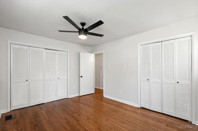 unfurnished bedroom with two closets, wood finished floors, baseboards, and visible vents
