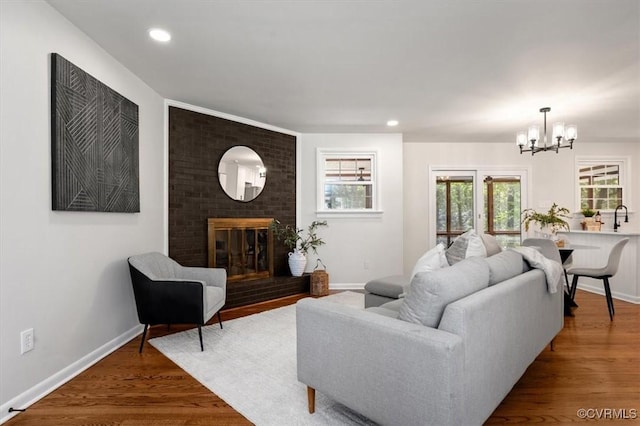 living room featuring baseboards, wood finished floors, a notable chandelier, and a brick fireplace