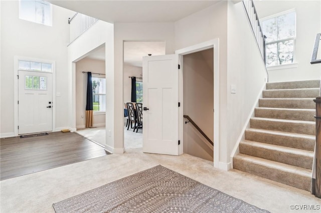 carpeted entrance foyer featuring stairway, baseboards, and plenty of natural light