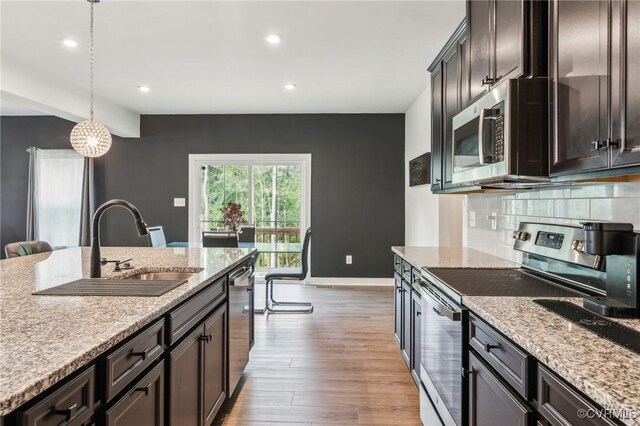 kitchen with stainless steel appliances, a sink, baseboards, light wood-style floors, and decorative backsplash