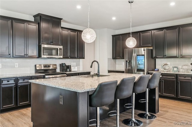 kitchen featuring light stone counters, stainless steel appliances, a sink, decorative backsplash, and a kitchen island with sink