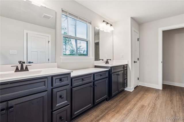 bathroom with a sink, wood finished floors, double vanity, baseboards, and visible vents