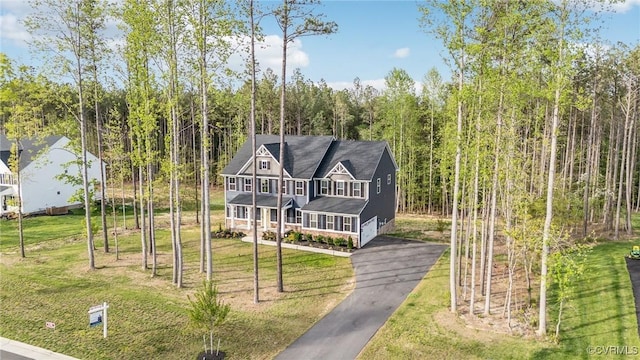 view of front of property with a view of trees, a porch, a front lawn, and aphalt driveway