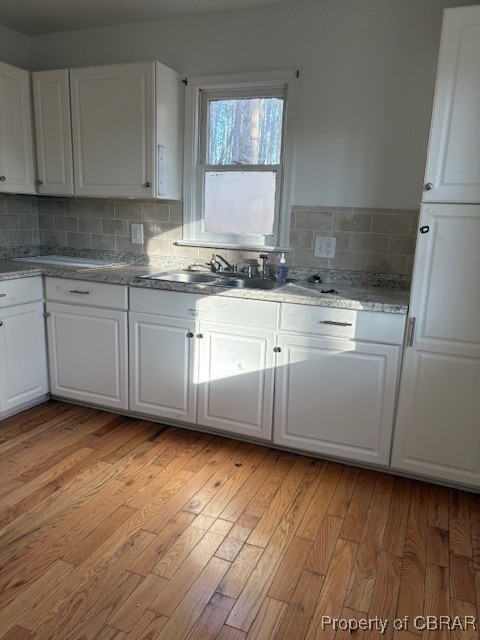 kitchen with white cabinetry, a sink, backsplash, and light wood finished floors