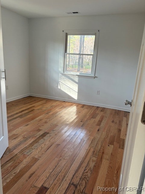 unfurnished room with baseboards, visible vents, and hardwood / wood-style flooring