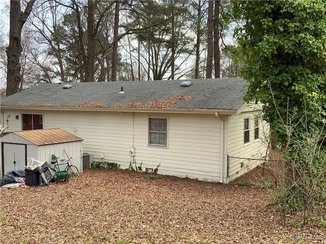 rear view of property featuring an outbuilding, a storage shed, fence, and roof with shingles