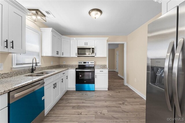 1713 Boydton Plank Rd, Petersburg, VA 23805 - kitchen with light stone countertops, stainless steel appliances, white cabinetry, a sink, and light wood-style floors