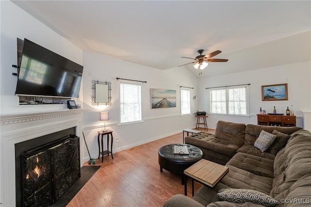 living area with a fireplace with flush hearth, ceiling fan, a wealth of natural light, and wood finished floors