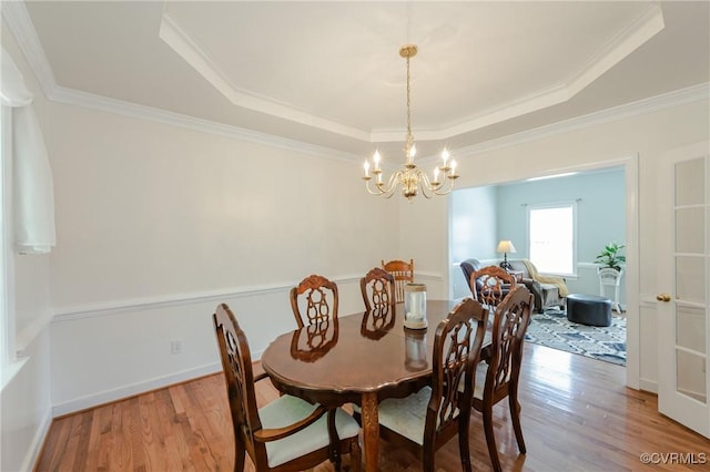 dining area featuring light wood-style flooring, a tray ceiling, a notable chandelier, and ornamental molding