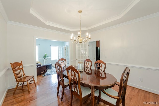 dining space with crown molding, a chandelier, light wood-style flooring, baseboards, and a raised ceiling