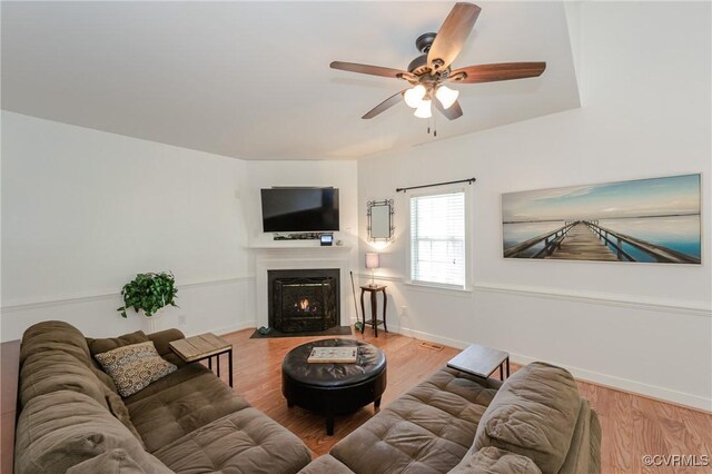 living area with a fireplace with flush hearth, wood finished floors, a ceiling fan, and baseboards
