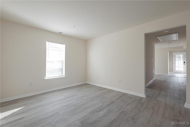 empty room featuring baseboards, visible vents, wood finished floors, and attic access