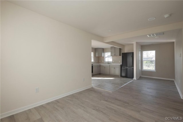 unfurnished living room featuring a sink, baseboards, visible vents, and wood finished floors