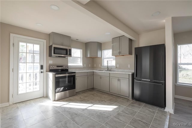 kitchen with a sink, gray cabinets, light countertops, and appliances with stainless steel finishes