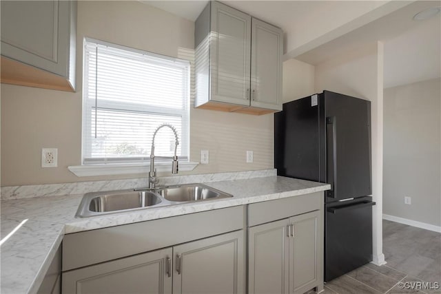 kitchen featuring light countertops, gray cabinets, baseboards, a sink, and freestanding refrigerator