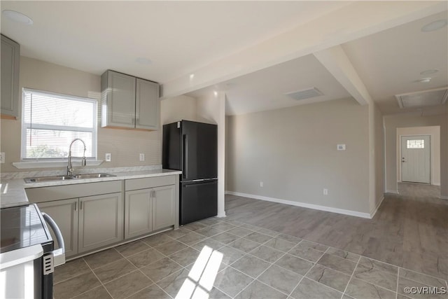 kitchen with light countertops, a sink, freestanding refrigerator, baseboards, and decorative backsplash