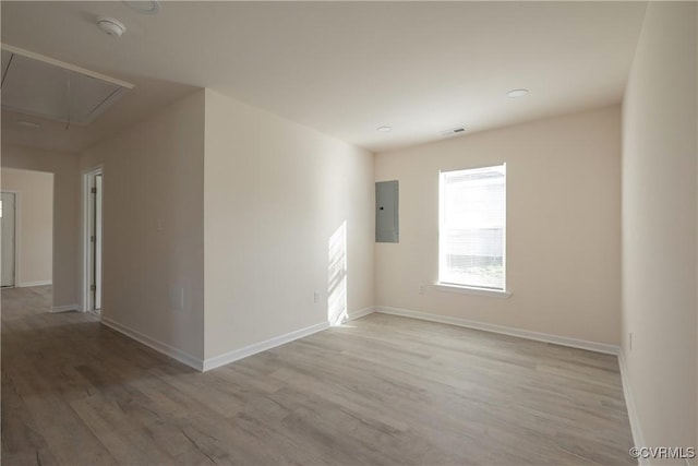 unfurnished room featuring light wood-style floors, visible vents, electric panel, and attic access