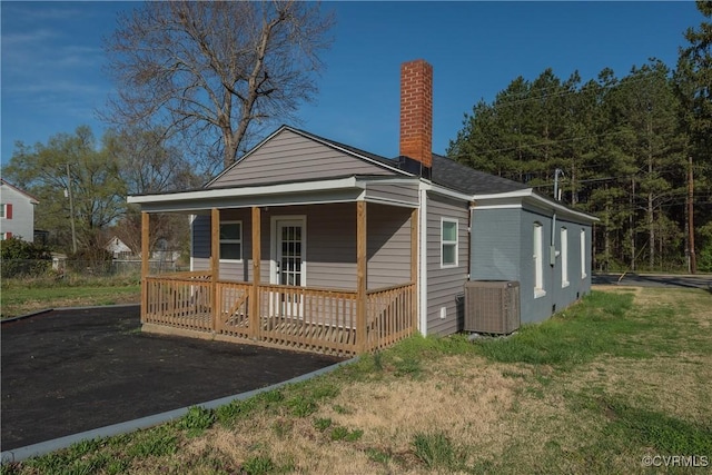 rear view of house with fence, a lawn, central AC unit, covered porch, and a chimney