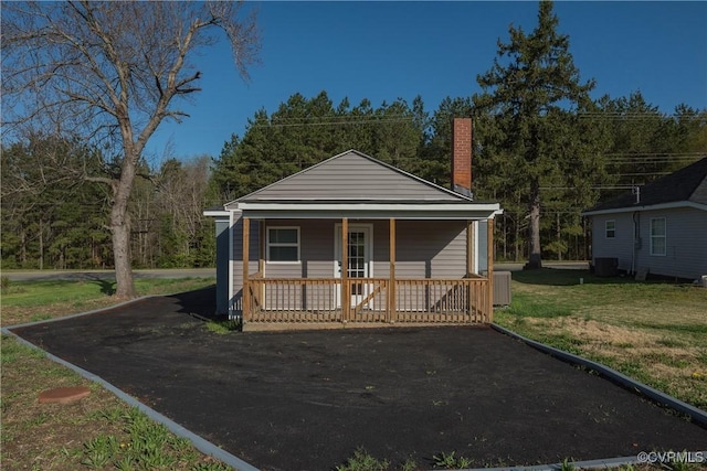 view of front of property with cooling unit, a chimney, a front lawn, and a porch