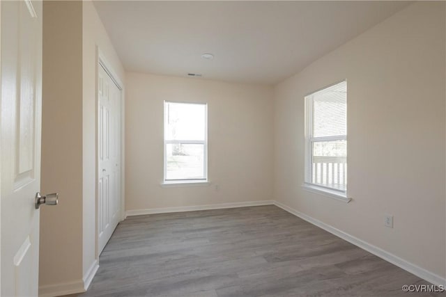 spare room with baseboards, visible vents, wood finished floors, and a healthy amount of sunlight
